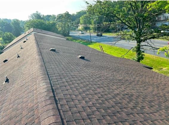 Brown shingled roof with multiple vent pipes, viewed from an angle against a sunny outdoor backdrop.