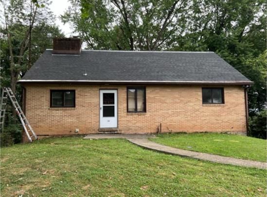 Single-story brick house with dark roof and brown-framed windows. White front door, green lawn.