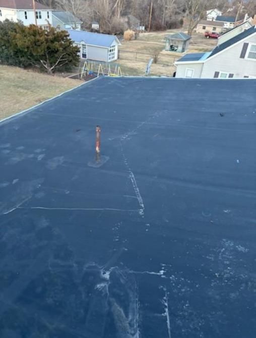 Black flat roof with some ice/water patches. Small antenna and residential buildings in the background.