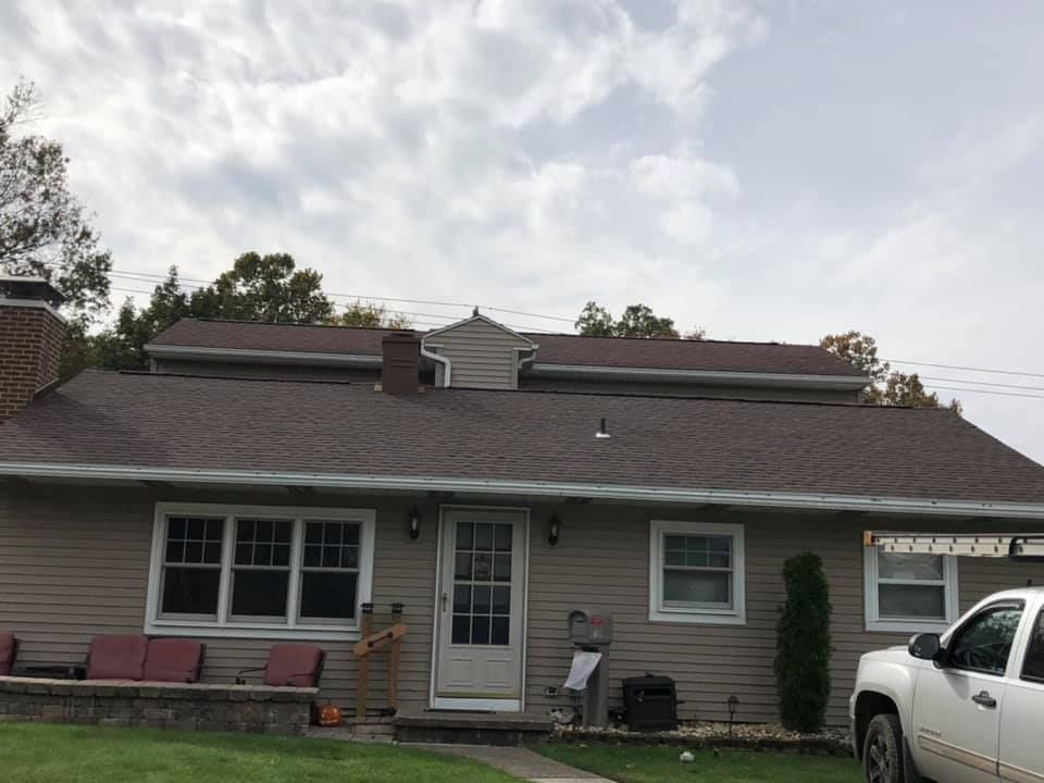 Brown-roofed house with beige siding, white trim, and a truck parked outside on a cloudy day.