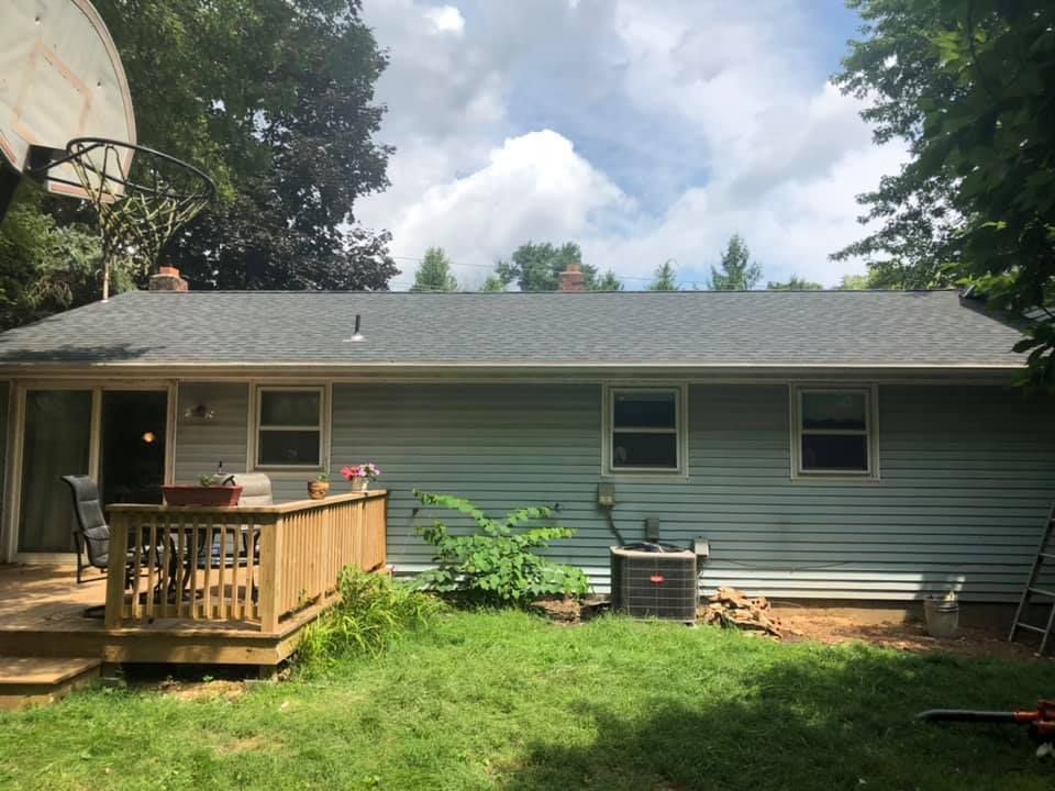 Back of a house with a gray roof and light blue siding, a wooden deck, and a basketball hoop.