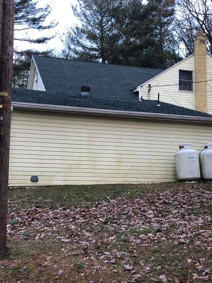Exterior of a house with yellow siding and a dark green roof. Propane tanks sit outside.