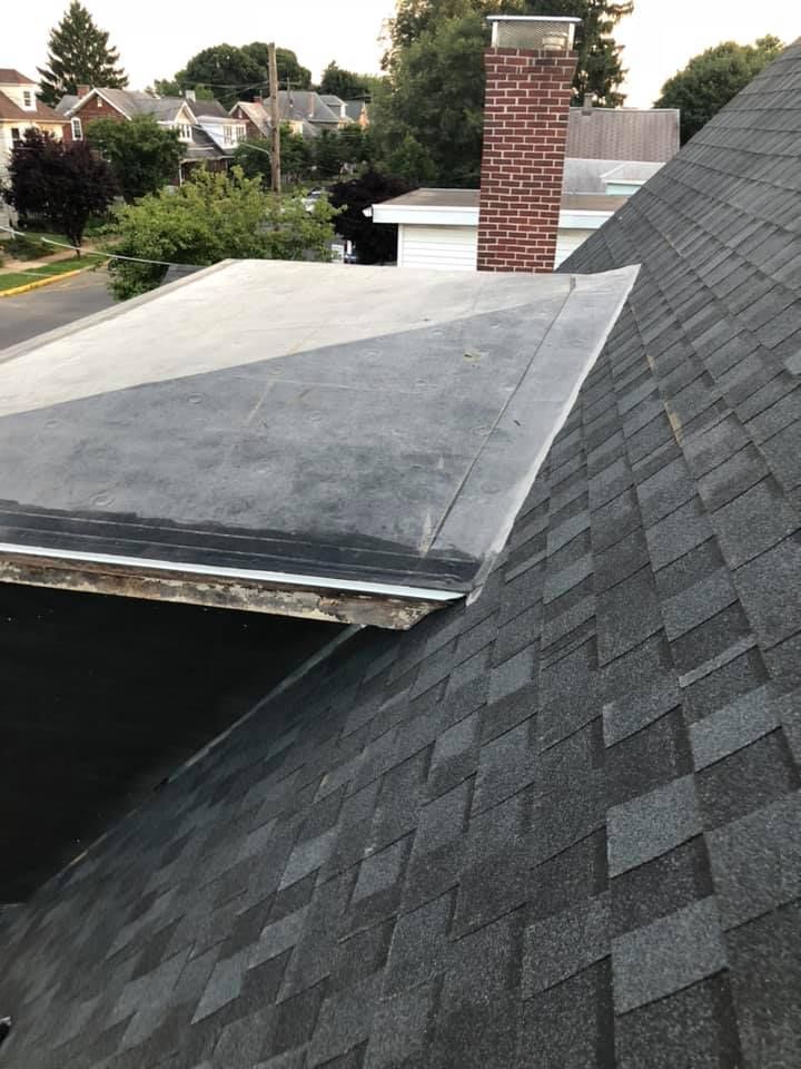 A roof with dark shingles meets a flat, gray roof; a brick chimney rises behind them.