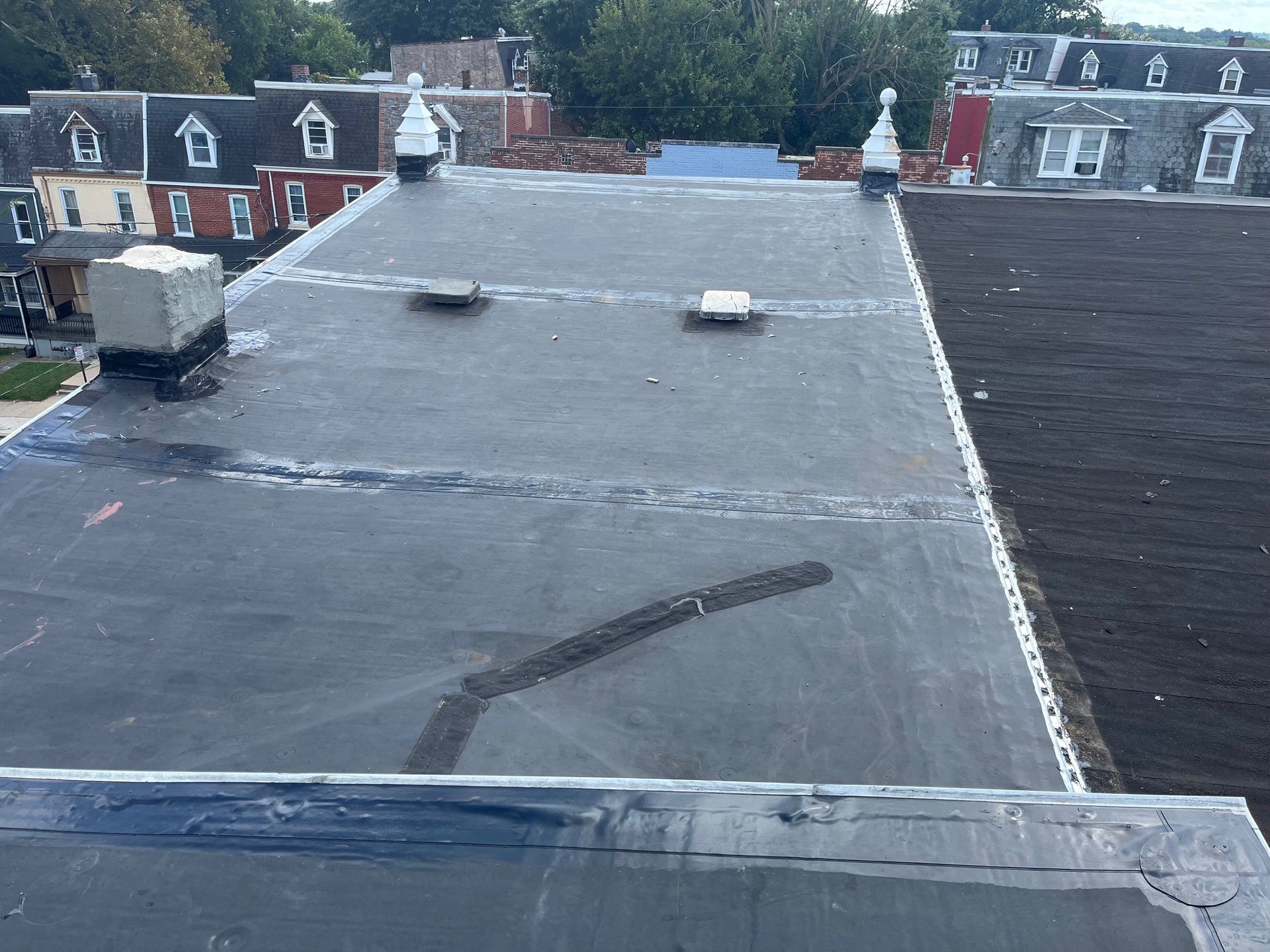 House with new black roof, beige siding, brick facade, black shutters, blue sky.