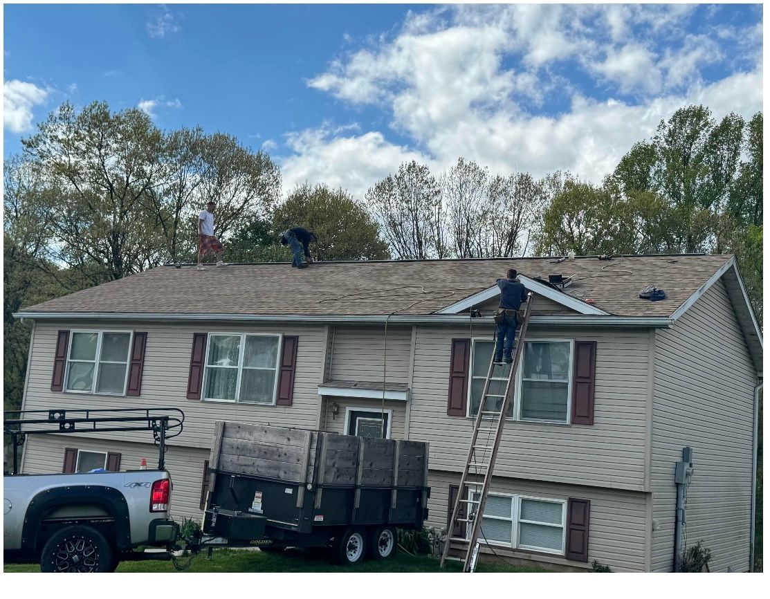 Roof with brown shingles, a dome vent, and a flat tar surface. Houses and trees in the background.