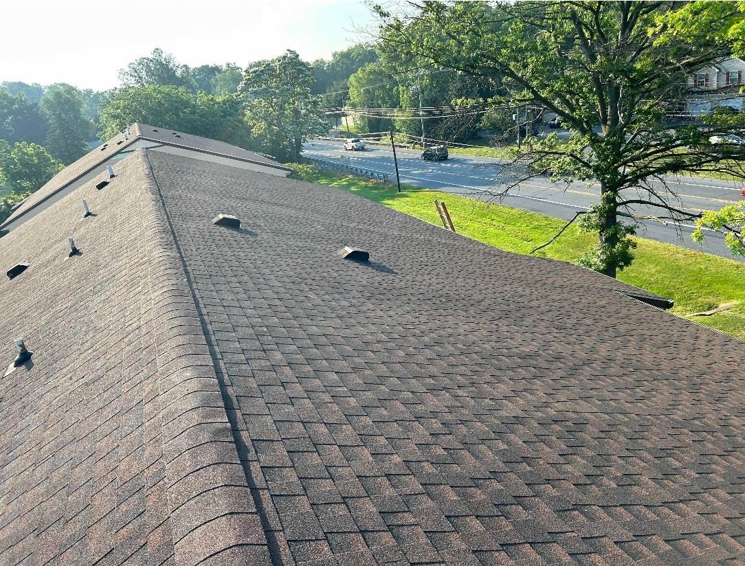 Brown shingle roof with several vents, overlooking a road and trees.