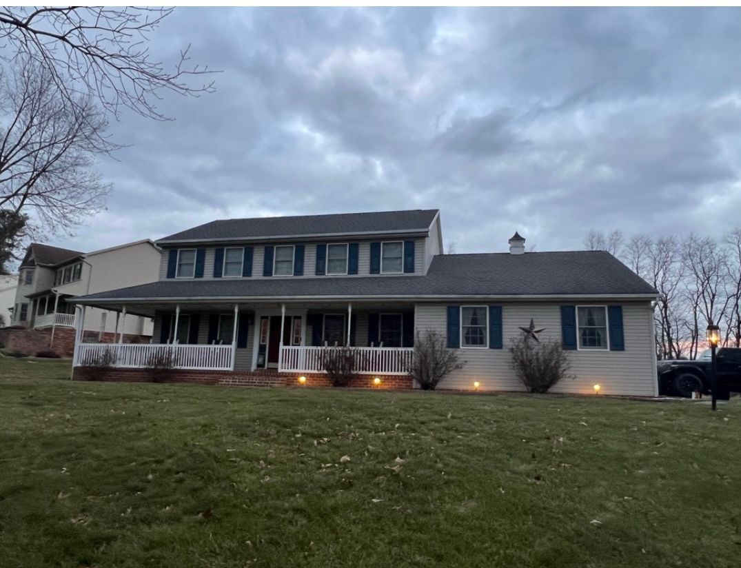 Two-story house with a large porch, blue shutters, and cloudy sky.