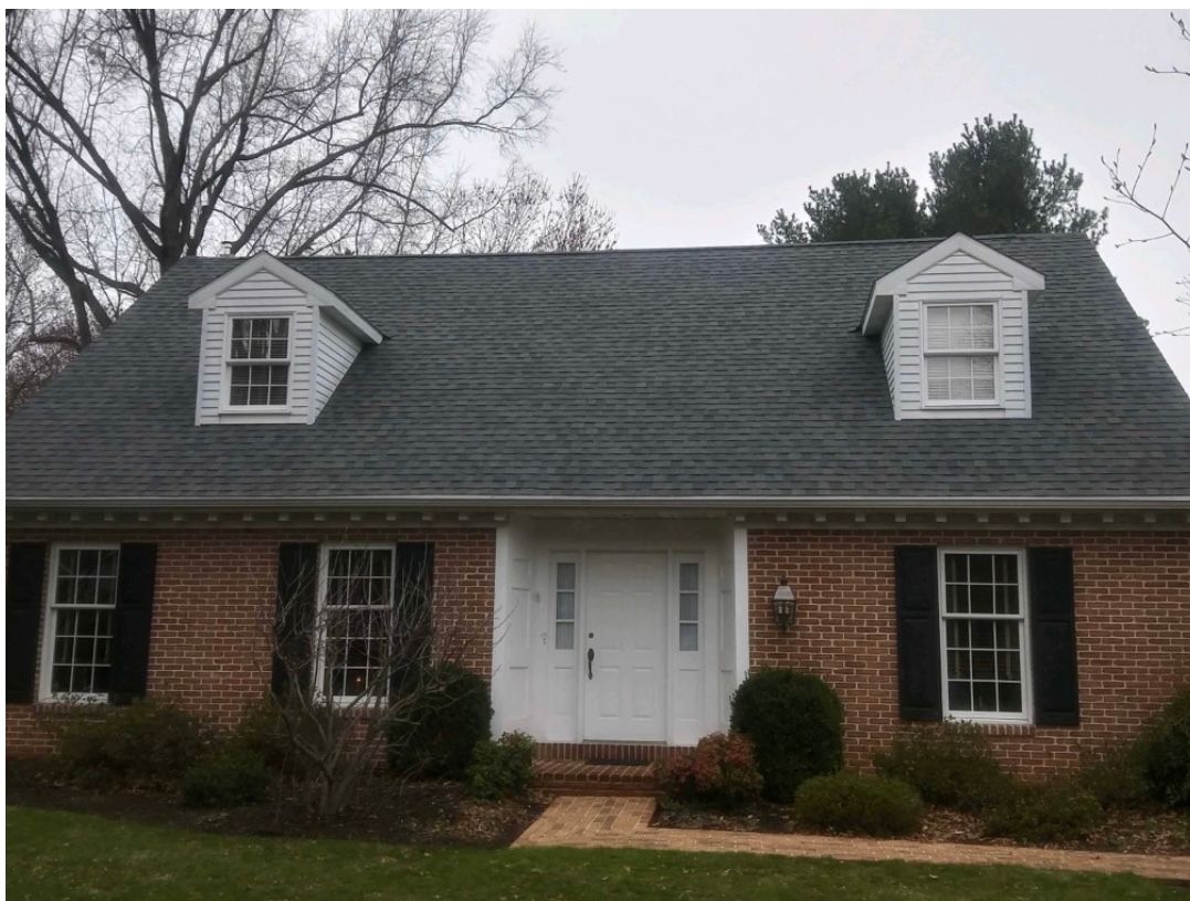 Brick house with a gray roof and white dormers, door, and window trim; black shutters.