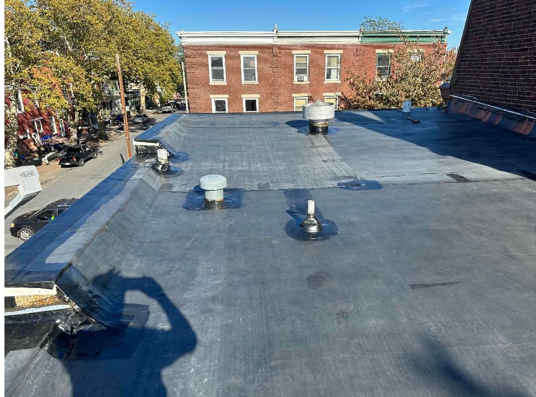 Black, flat roof with vents and buildings in background.