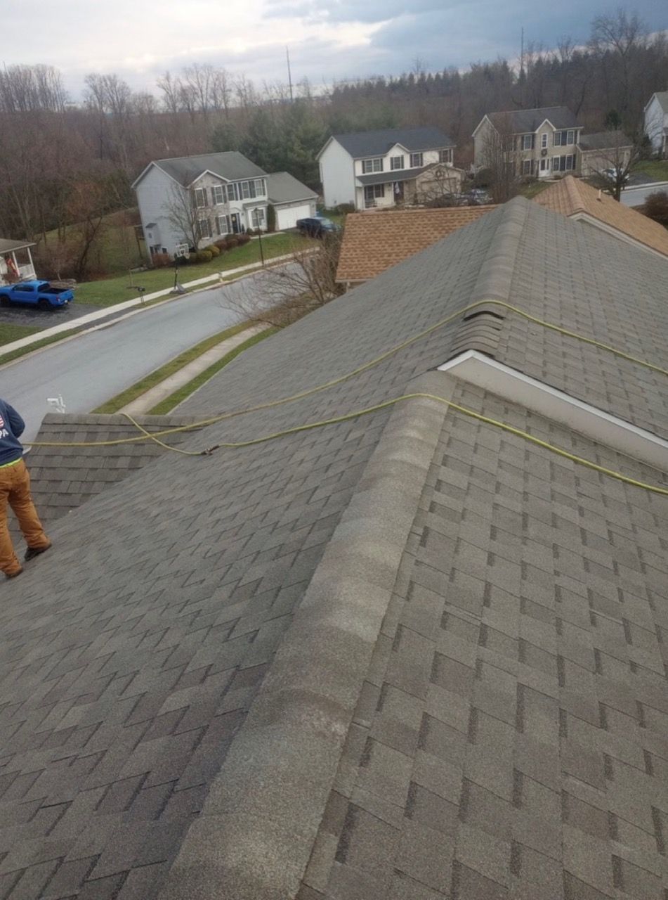 Person standing on a gray shingled roof, looking towards a residential street with houses.