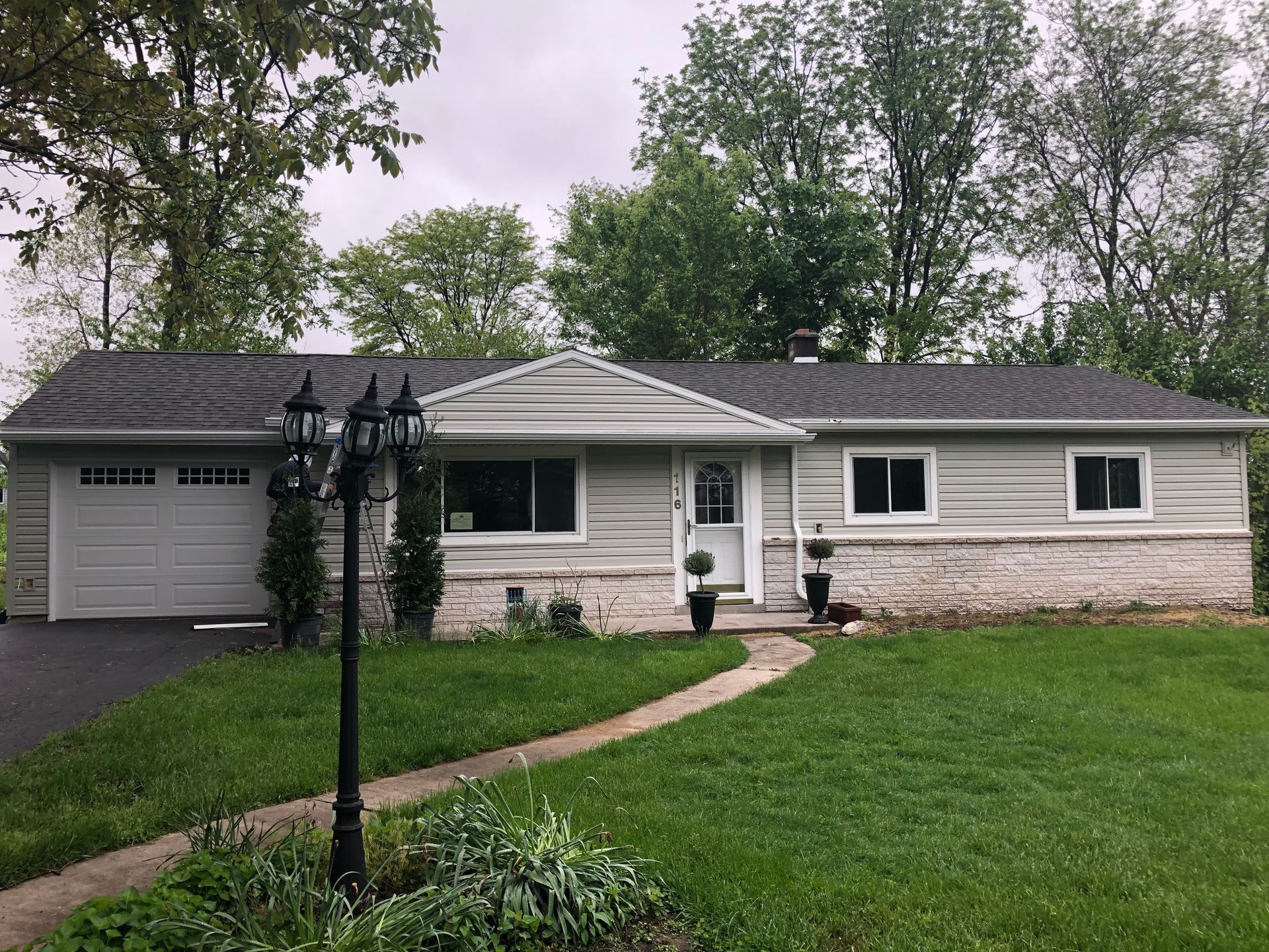 Ranch-style house with gray siding, white trim, and a brick foundation. A pathway leads to the front door.