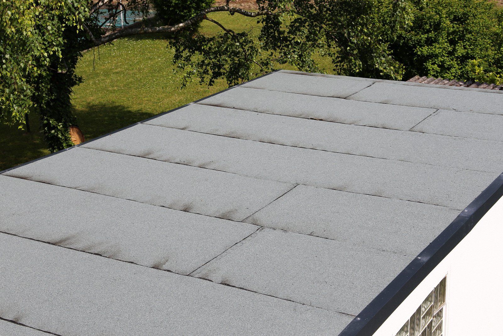 Grey rectangular roof tiles on a flat roof, green trees in background.