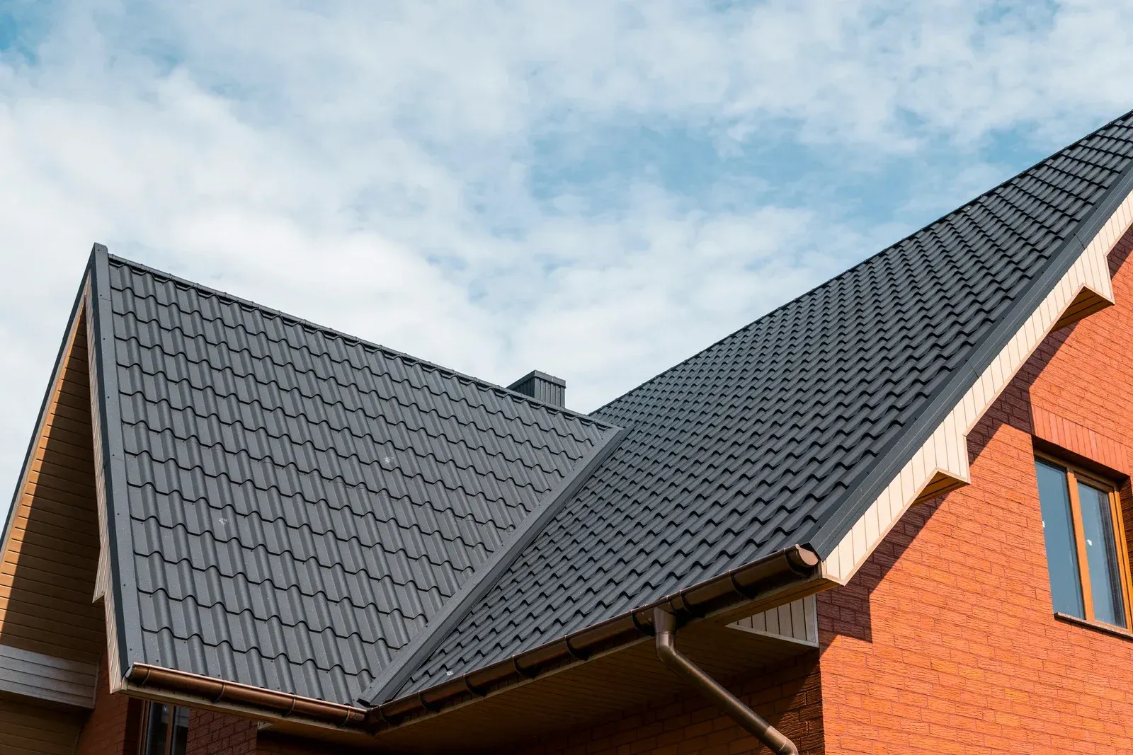 Black metal roof on a brick building, blue sky backdrop.