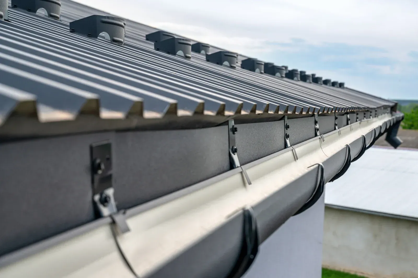 Gray metal roof with matching gutters, seen from below, against a cloudy sky.