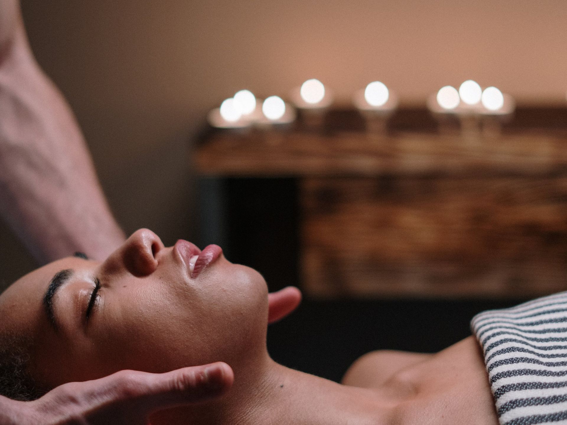 Persona recibiendo un masaje facial. Manos en la cara, velas al fondo.