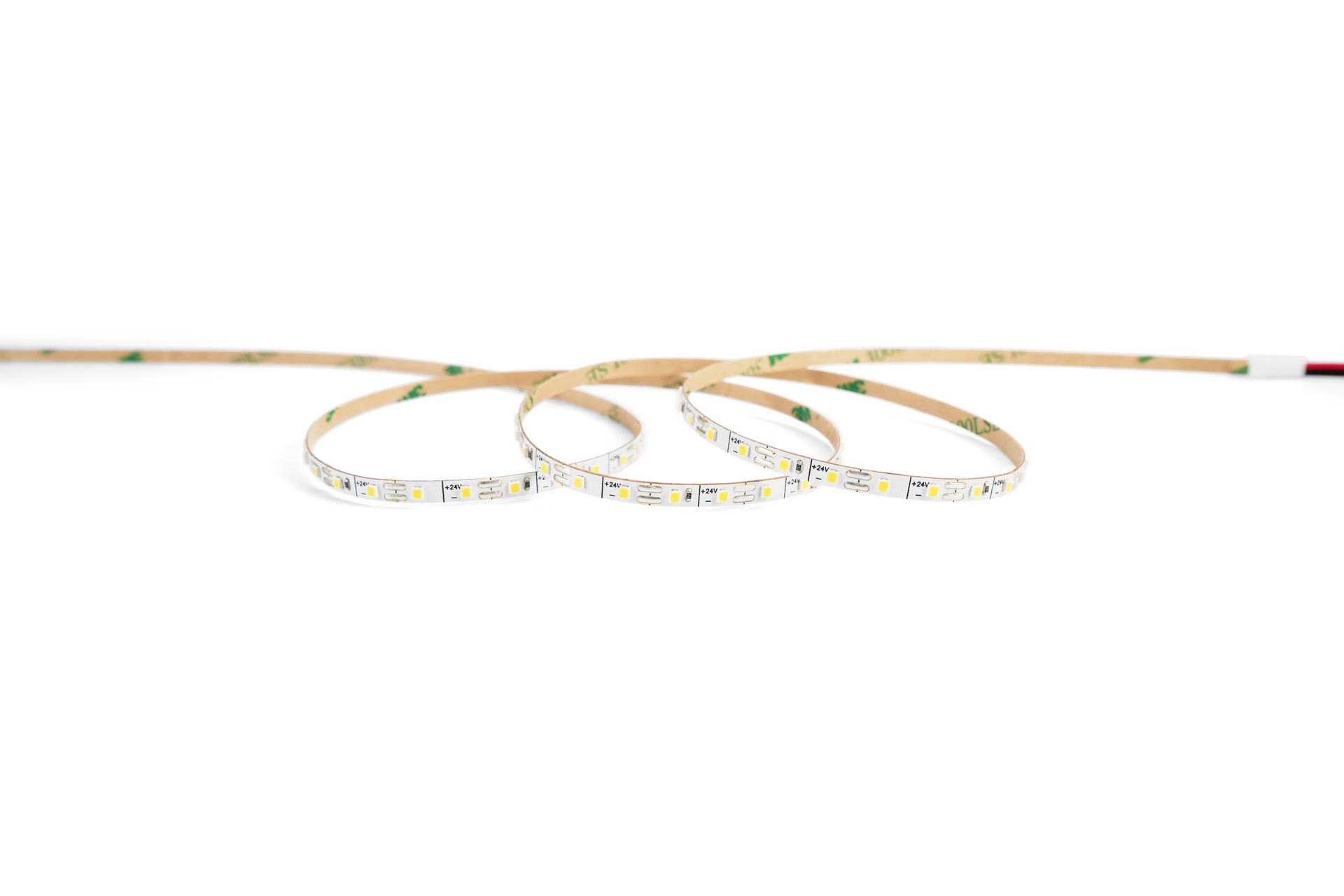 LED light strip with adhesive backing, coiled on a white surface.