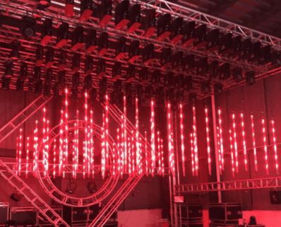 Red stage lighting setup with hanging vertical lights and overhead spotlights.