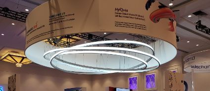 A circular display with glowing rings, hanging from the ceiling, with text and a trade show setting.