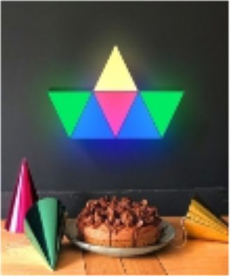 A colorful, geometric wall light above a birthday cake and party hats.