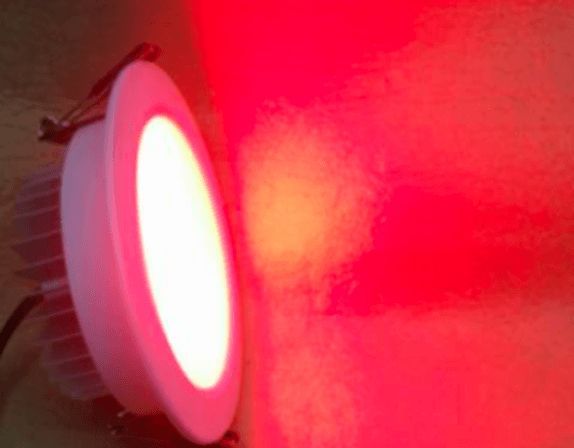 A round, white LED light fixture illuminates a red wall.