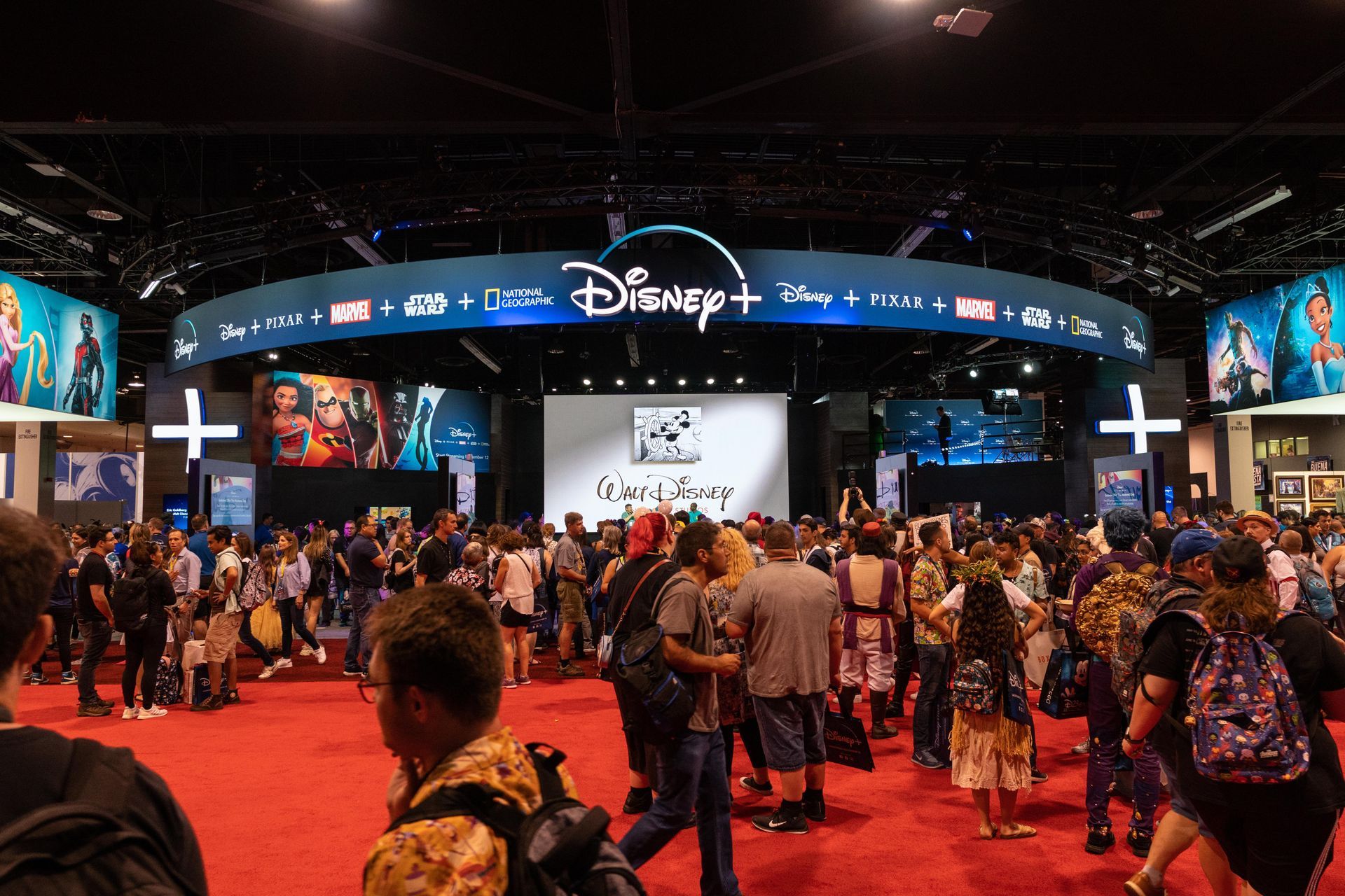 A crowd of people are gathered in a room with a sign that says disney +