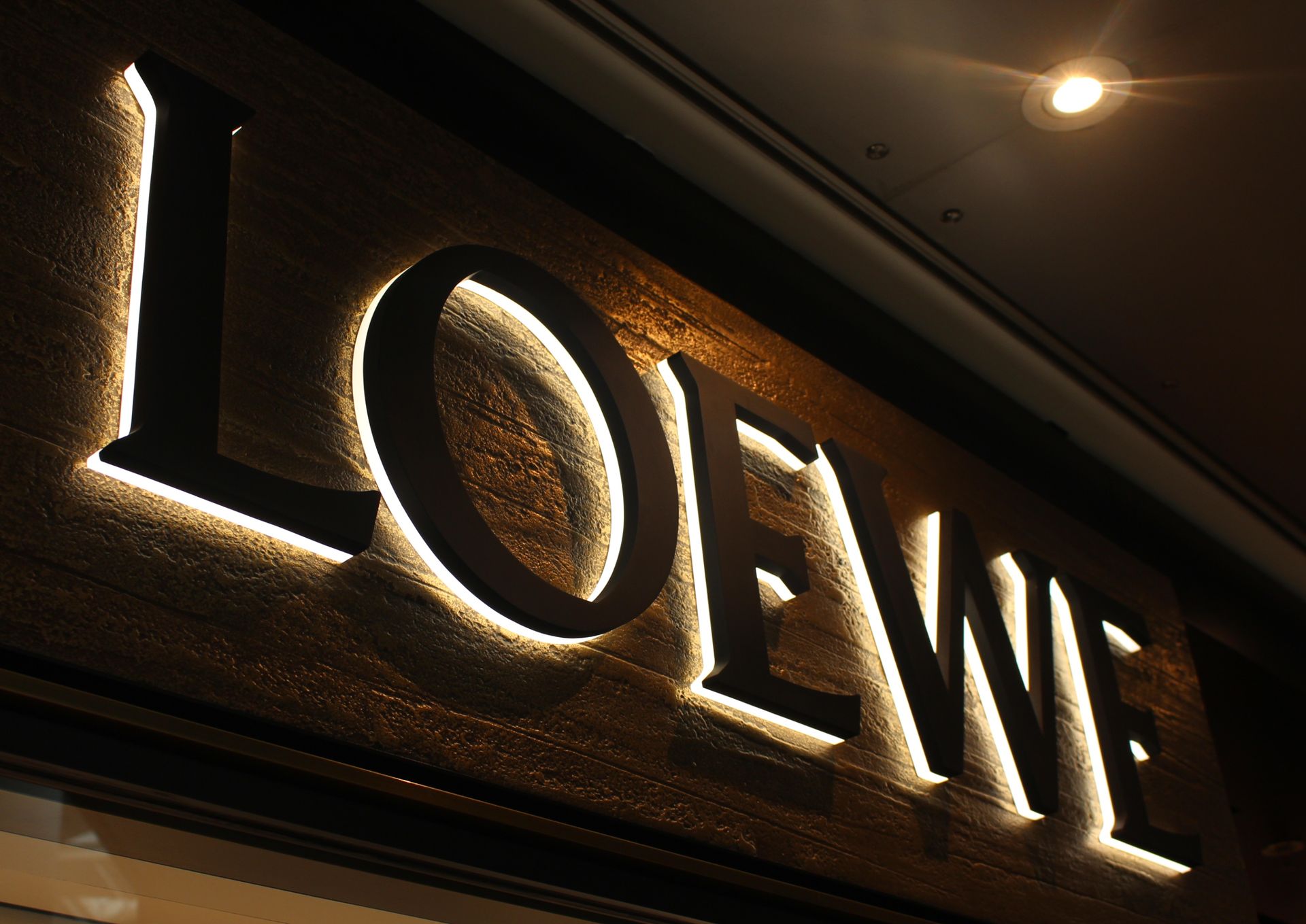 Illuminated Loewe sign with black letters and gold backlighting.