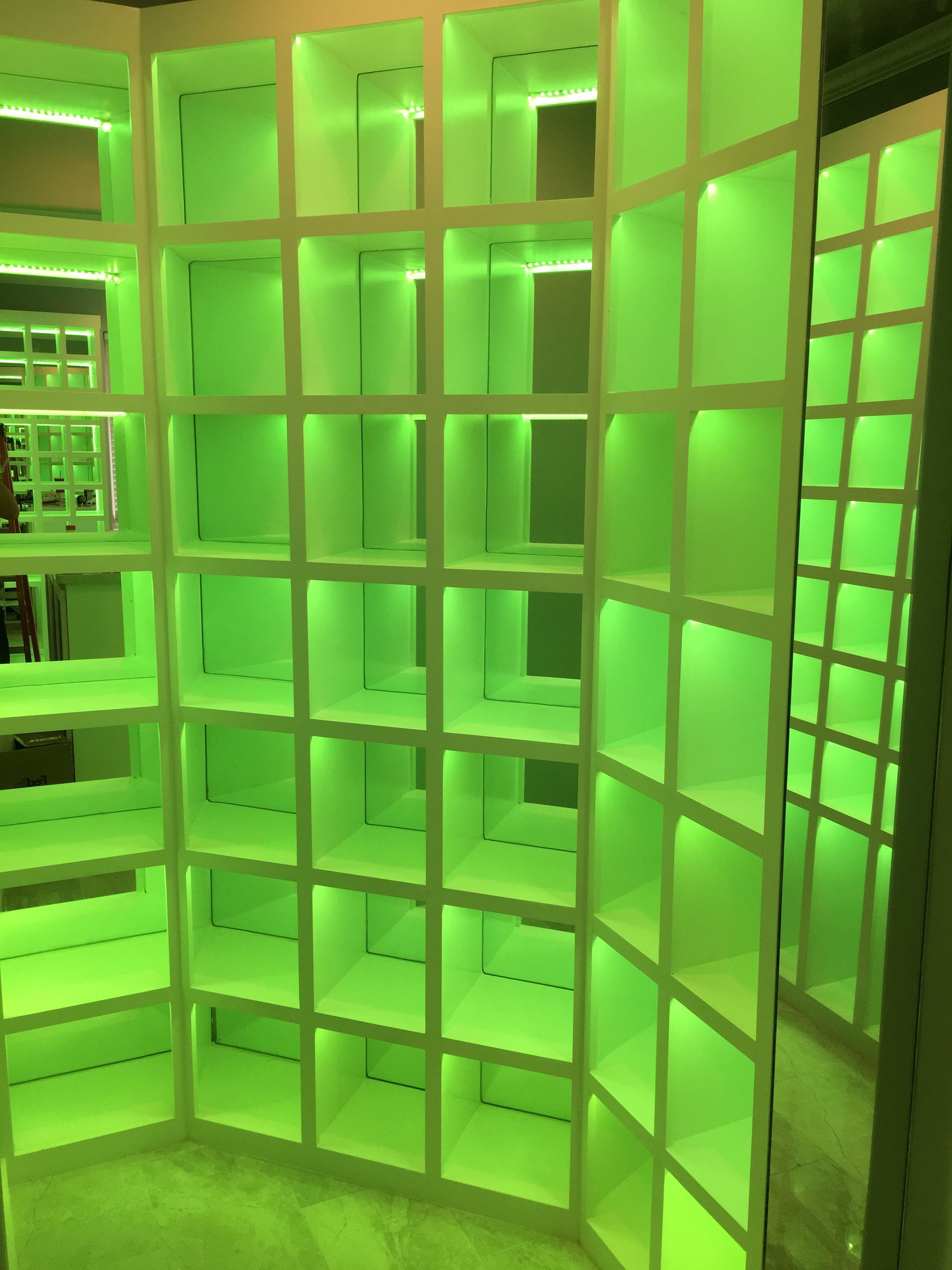 A closet with green lights on the shelves and a mirror.