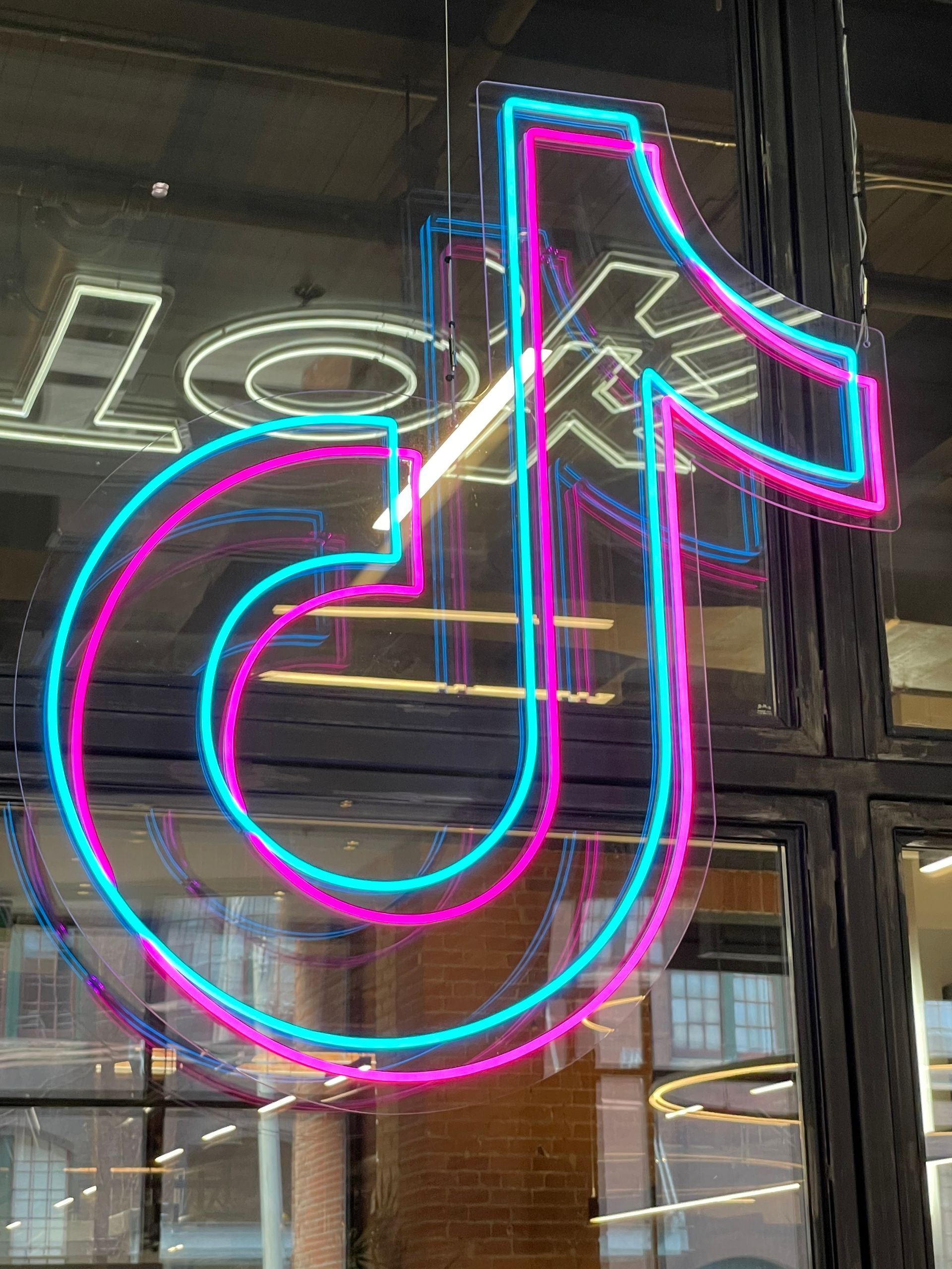 Neon TikTok logo in blue and pink against a window.