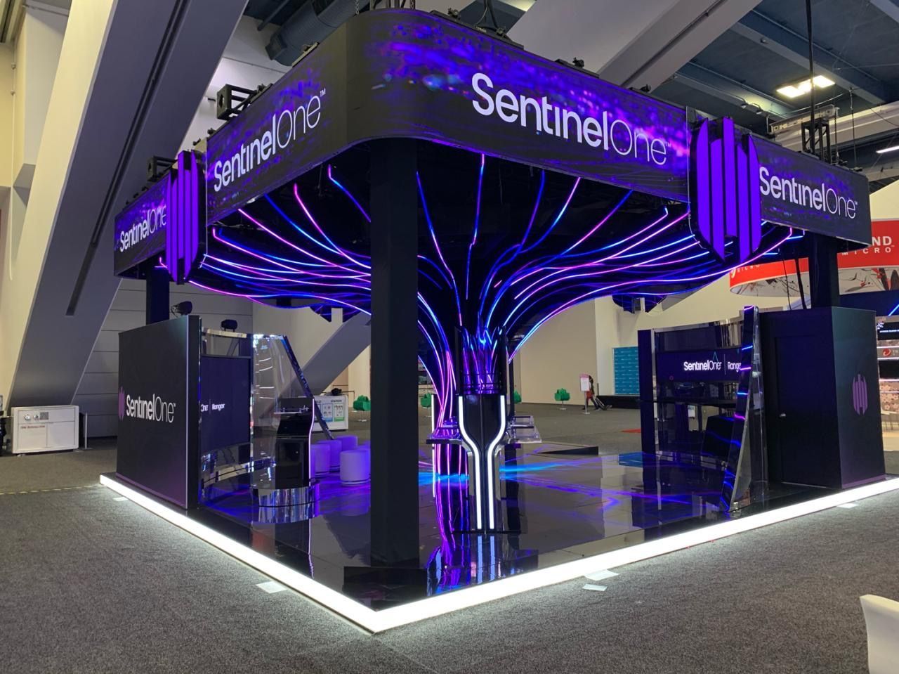 SentinelOne booth at a convention, featuring purple and white lights, shiny black surfaces, and the company logo.