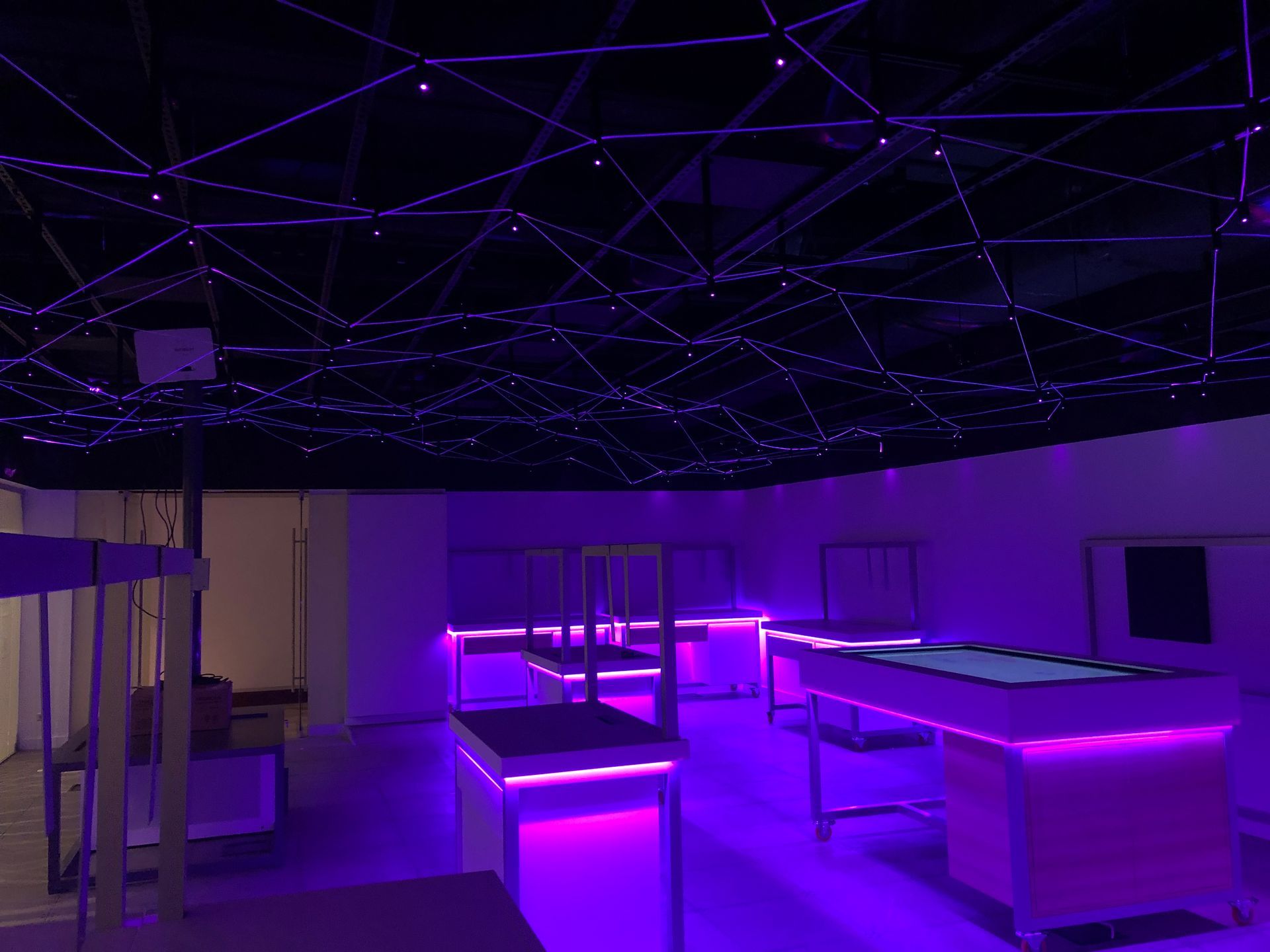 A room with purple lights on the tables and ceiling.