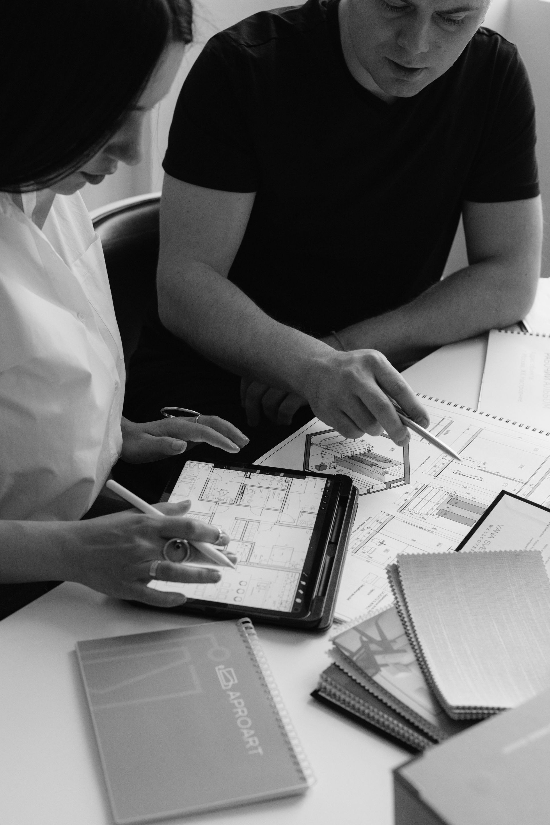 Two people looking at blueprints and a tablet on a table, discussing design details.