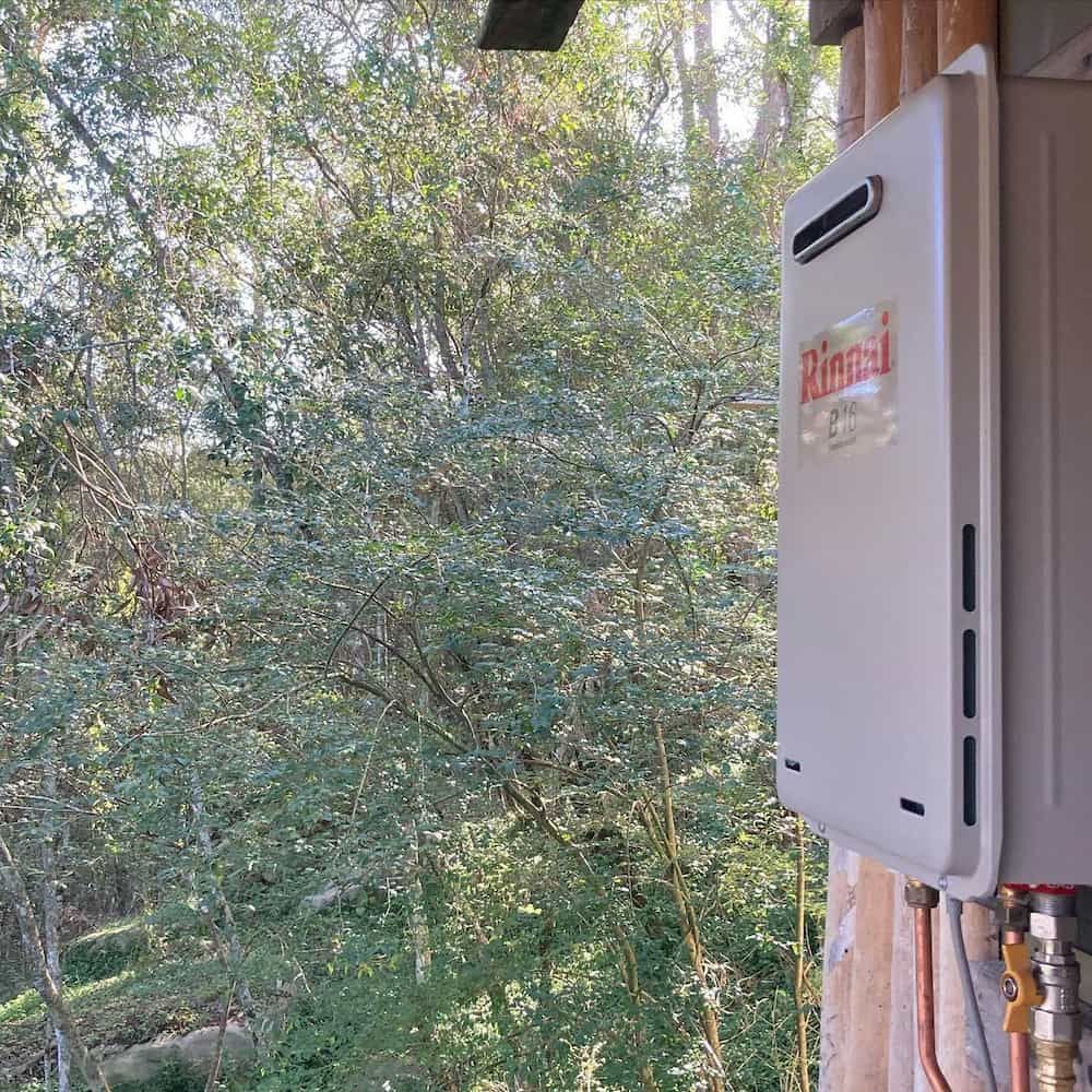 Rinnai Water Heater Mounted on a Building Exterior With Trees — Corrimal Plumbing Services in Shellharbour, NSW