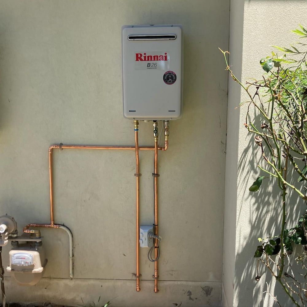 A Rinnai Tankless Water Heater Mounted on a Beige Exterior Wall — Corrimal Plumbing Services in Austinmer, NSW