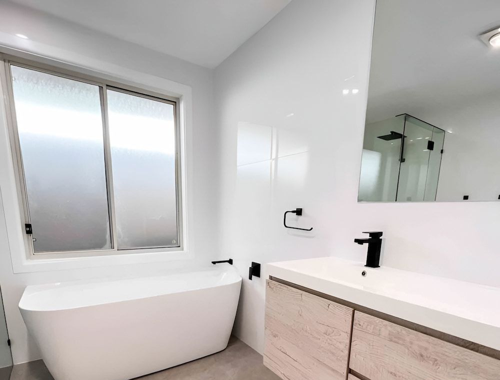 Modern Bathroom With White Tub, Vanity, and Large Window — Corrimal Plumbing Services in Thirroul, NSW