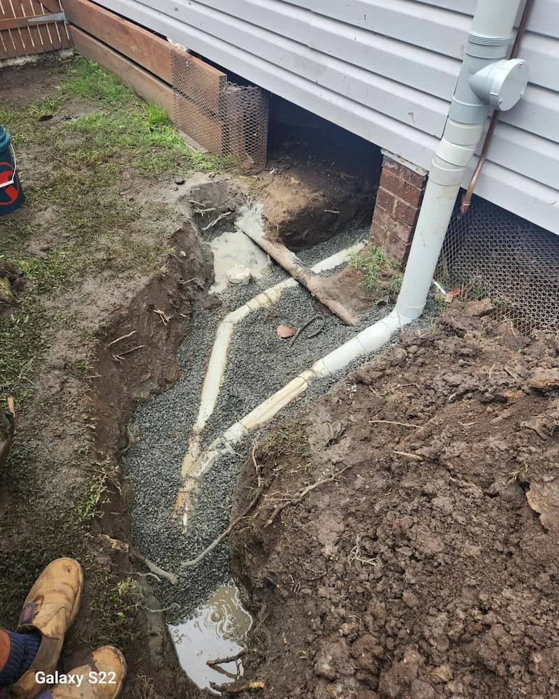 Trench Dug Around a House Foundation, Showing Drainage Pipes and Gravel — Corrimal Plumbing Services in Woonona, NSW