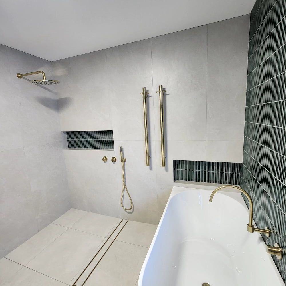 Bathroom With a White Bathtub, Gold Fixtures, and Grey and Green Tiles — Corrimal Plumbing Services in Woonona, NSW