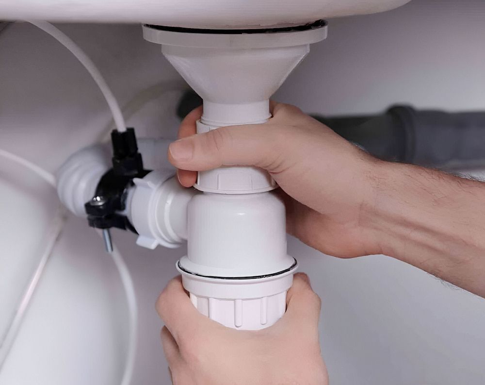 Hands Assembling White Plastic Sink Drain Pipes Under a White Sink — Corrimal Plumbing Services in Woonona, NSW