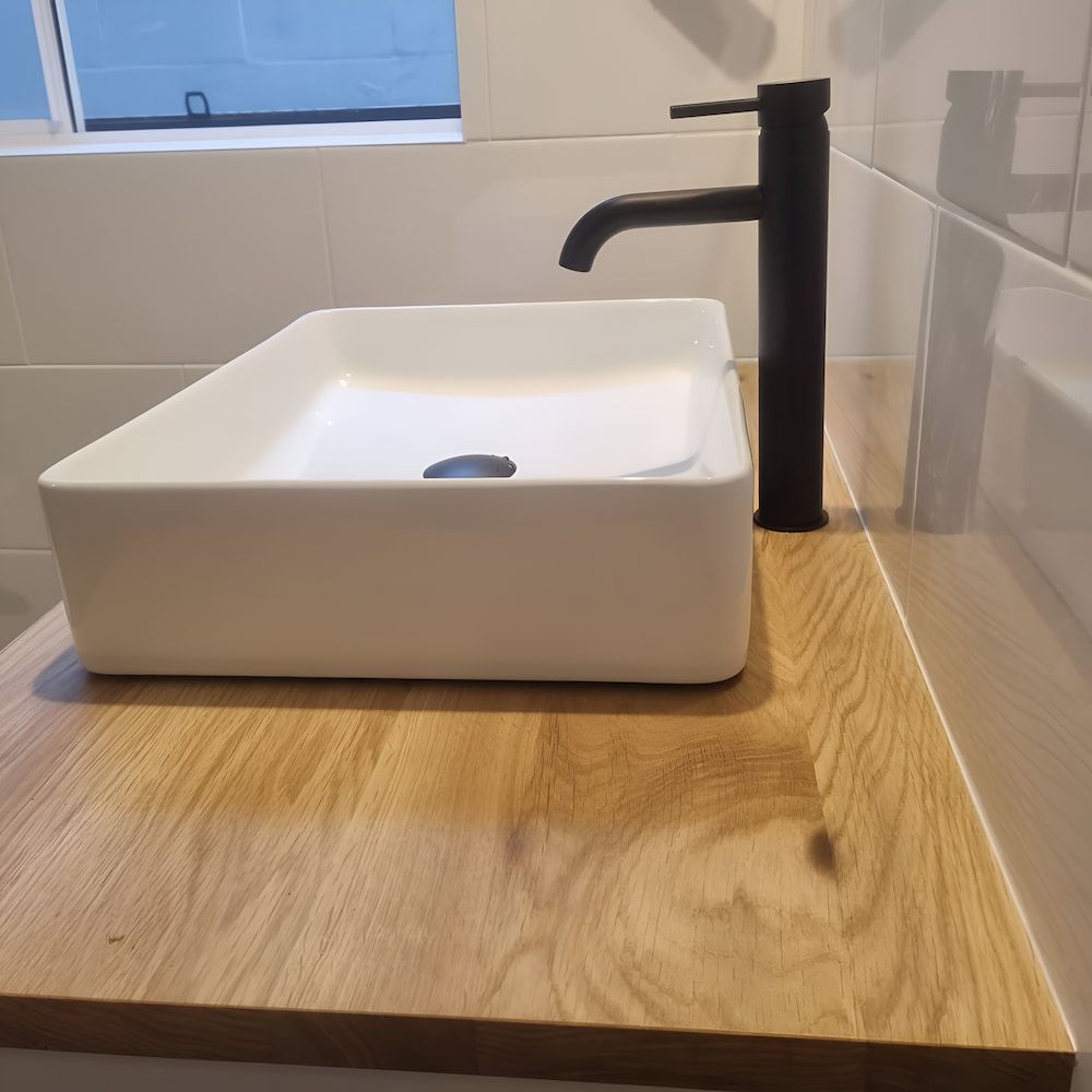 White Rectangular Bathroom Sink With Black Faucet on a Wooden Countertop — Corrimal Plumbing Services in Austinmer, NSW