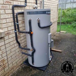 A Grey Hot Water Heater is Mounted Outside, With Black Pipes — Corrimal Plumbing Services in East Corrimal, NSW