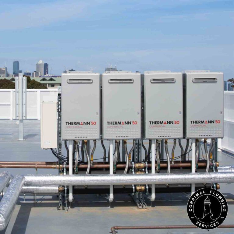 Four Grey Water Heaters on a Rooftop, With Copper Pipes and a City Skyline — Corrimal Plumbing Services in East Corrimal, NSW