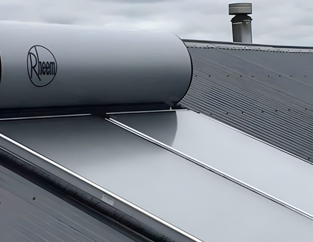 Rheem Solar Hot Water System on a Grey Metal Roof, With a Chimney — Corrimal Plumbing Services in Thirroul, NSW