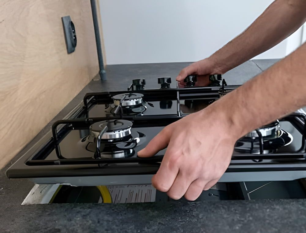 Hands Installing a Black Stovetop Into a Countertop — Corrimal Plumbing Services in East Corrimal, NSW