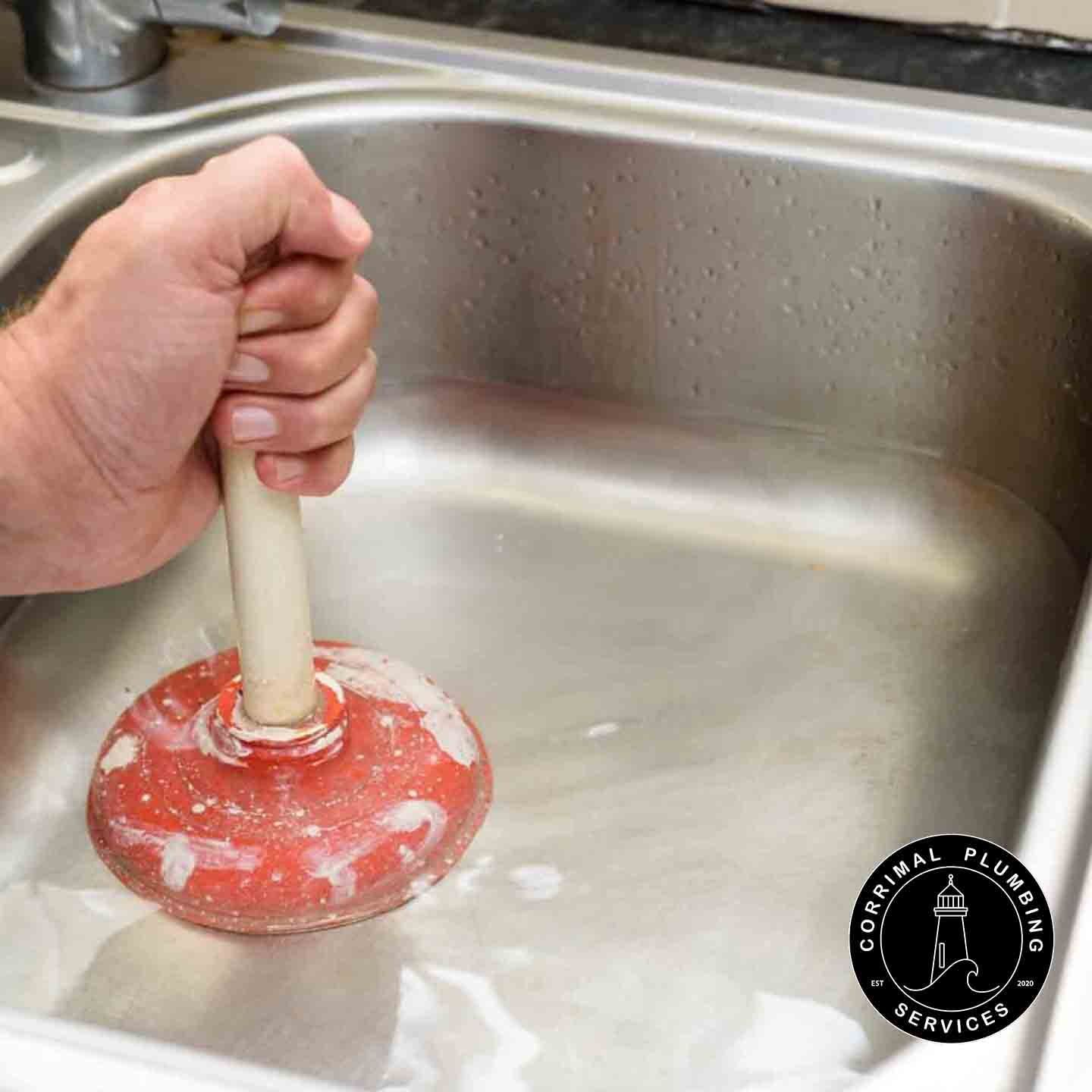 Hand Using a Red Plunger in a Silver Kitchen Sink Filled With Soapy Water — Corrimal Plumbing Services in East Corrimal, NSW