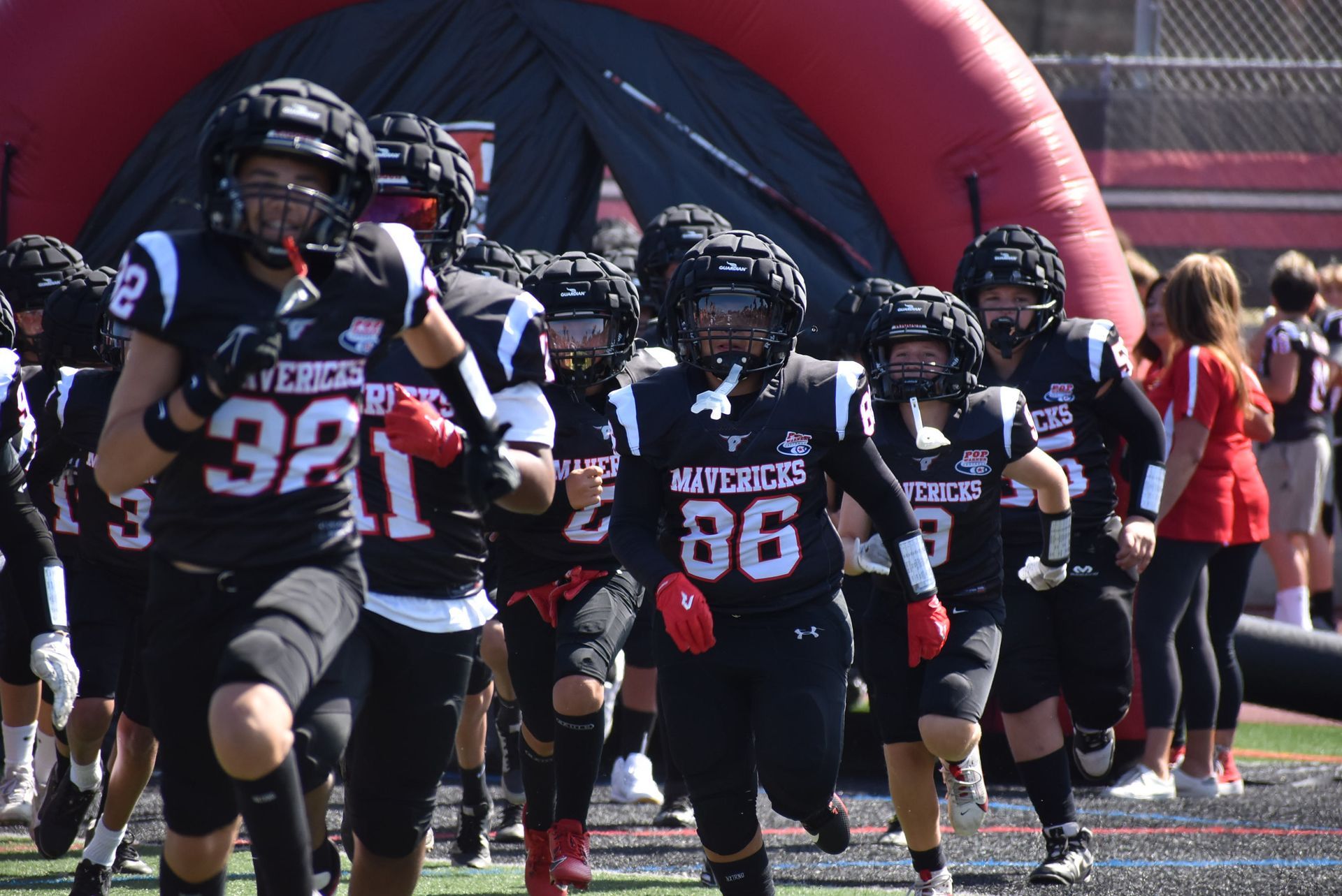 Football player in maroon jersey holding ball, smiling, surrounded by teammates on a field.