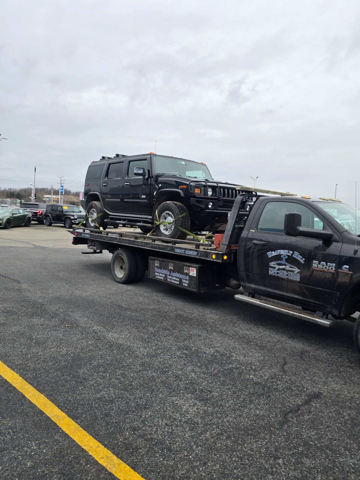 A black hummer is being towed by a tow truck in a parking lot.