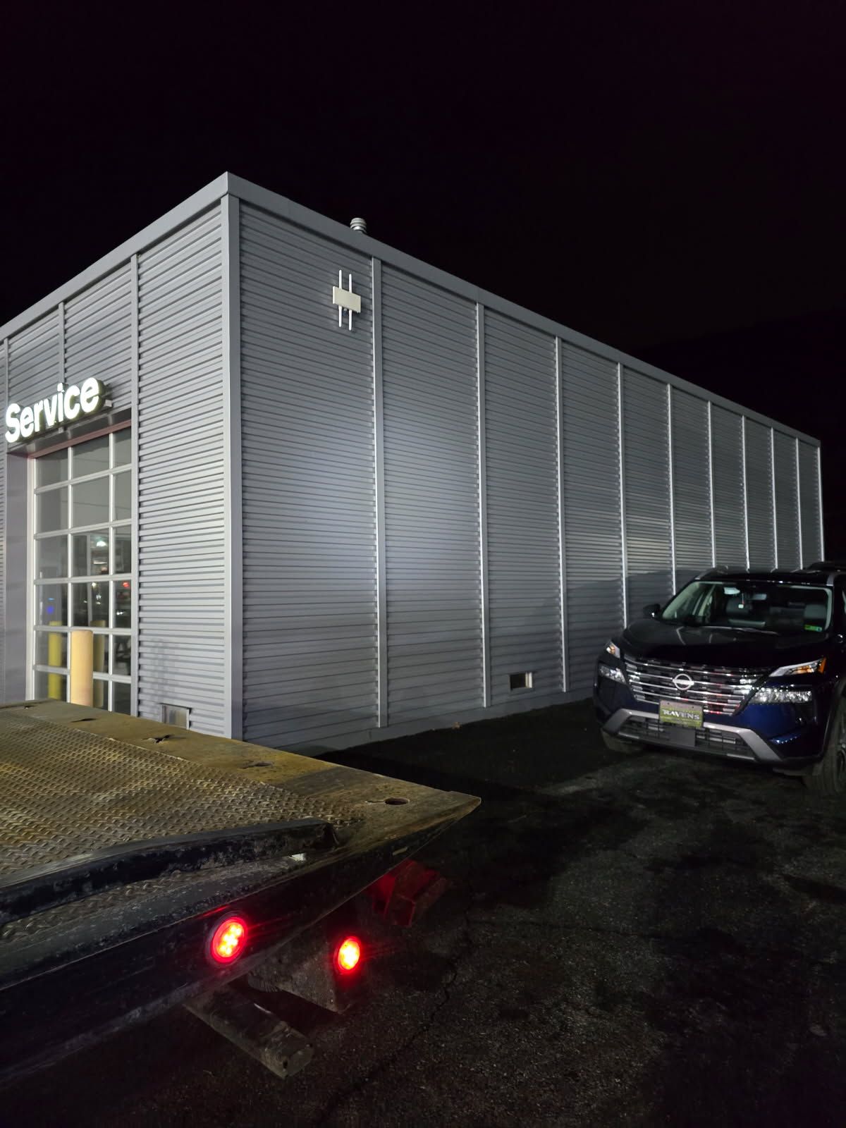 A car is parked in front of a service building at night.