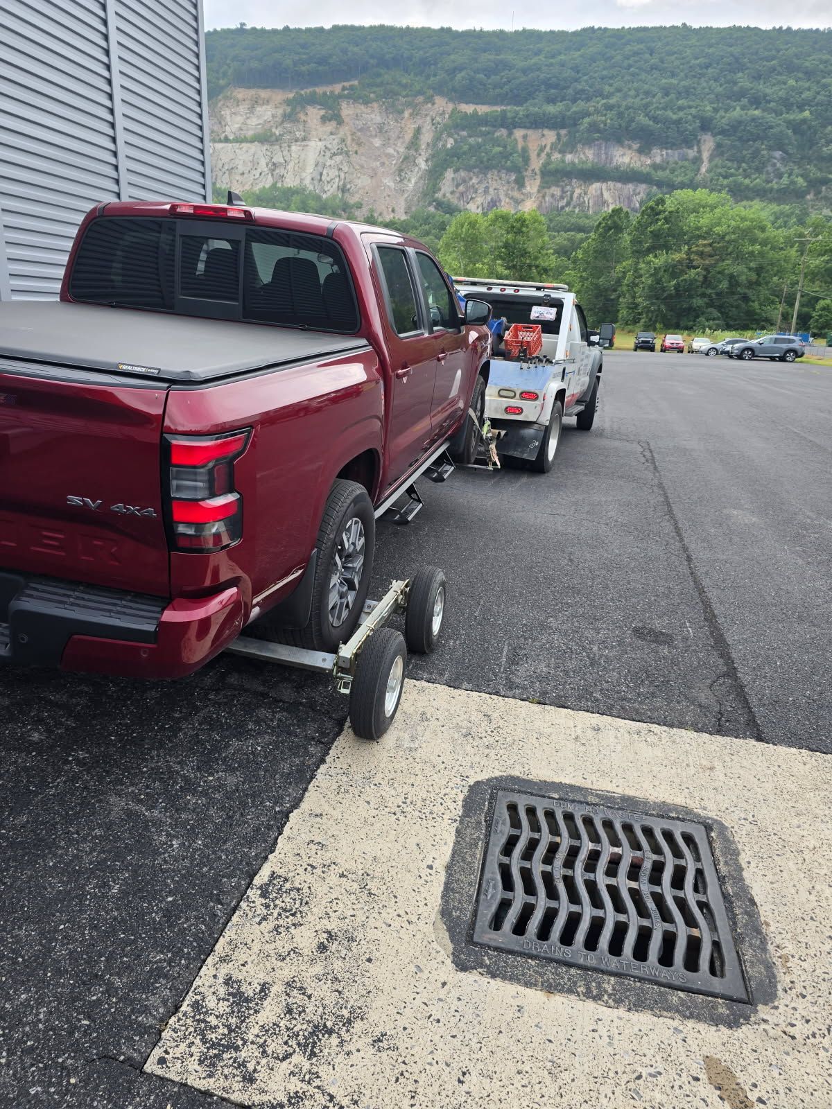 A red truck is being towed by a tow truck in a parking lot.