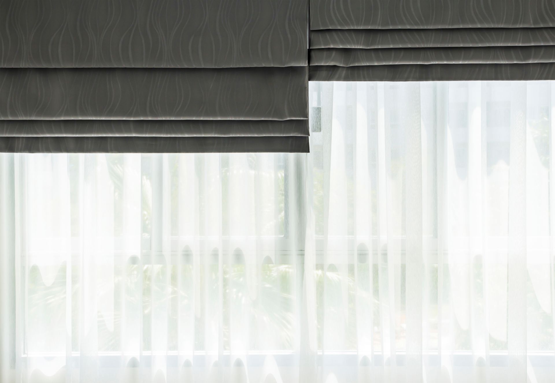 Gray Roman shade partially covering a window with sheer white curtains.