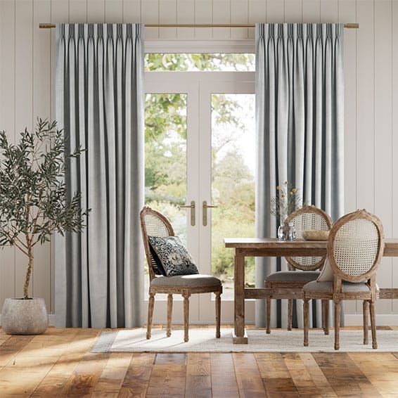 Dining room with curtains, table, chairs, and a plant next to a door with a view of trees.
