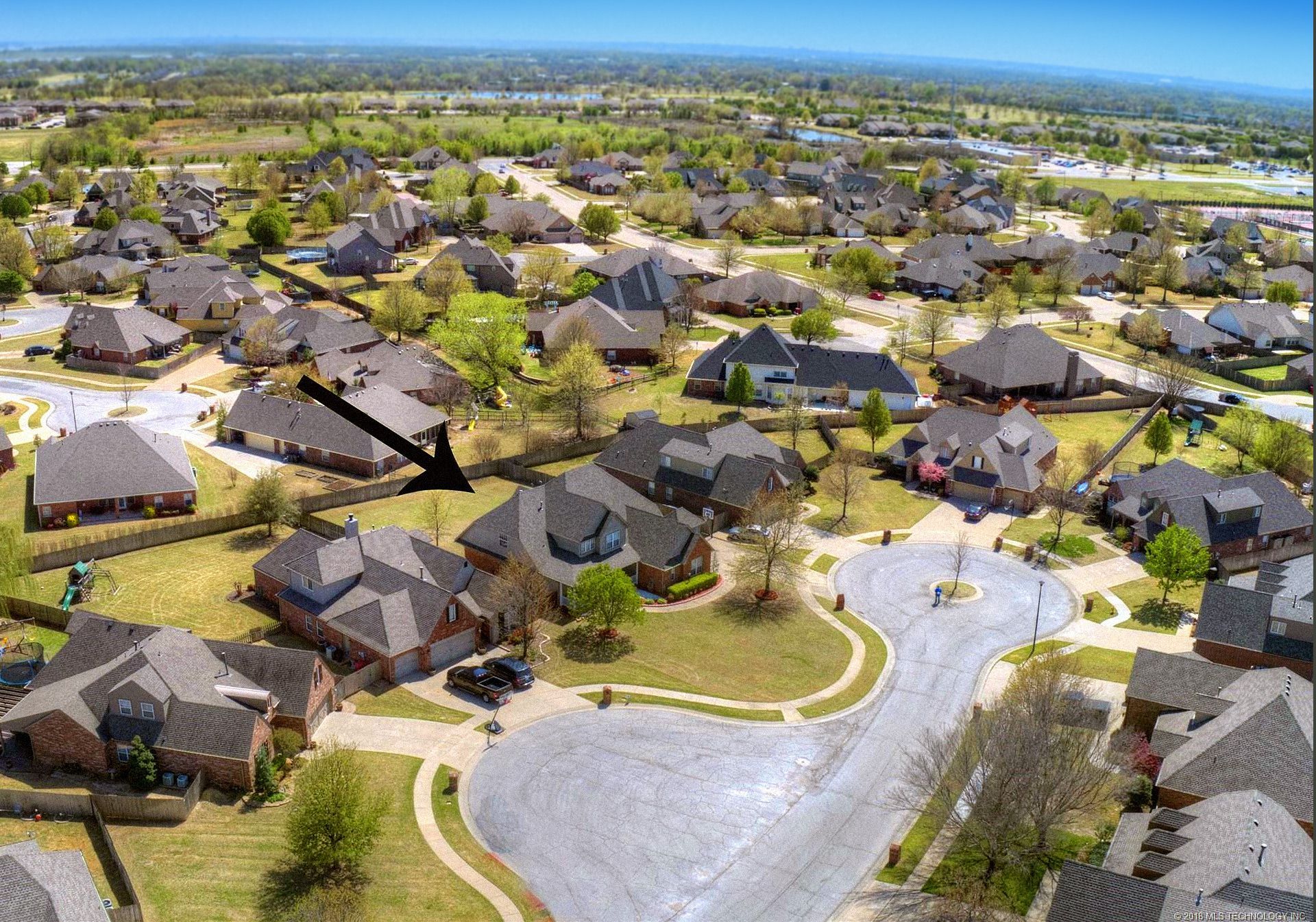 An aerial view of a residential area with a black arrow pointing to a house